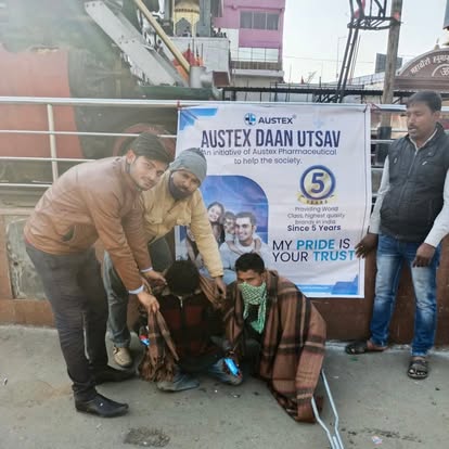 Austex volunteers wrapping a warm blanket around a man at a riverside ghat